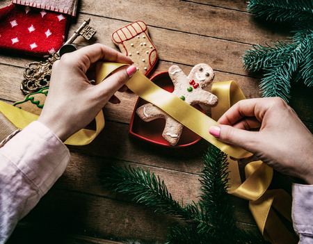 Young woman's hands wrapping Christmas gifts and cookies on wooden background, Photo in old color...