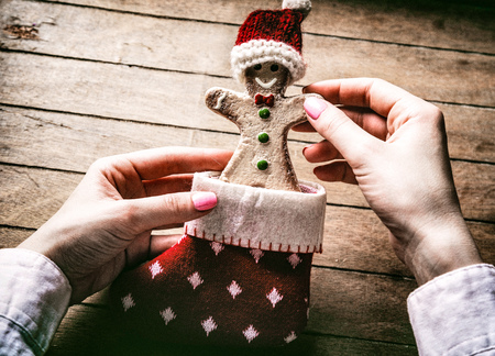 Young woman's hands holding Christmas gingerbread man cookie in sock on wooden background, Photo in old color image styleの写真素材