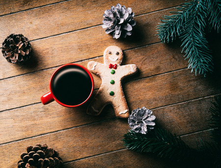 Cup of coffee and Christmas gingerbread man with pine cones and branches on wooden backgroundの写真素材