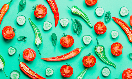 Above view at cutted chili pepper and basil with tomatoes and cucumbers on green background