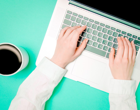 Female hands with cup of coffee and laptop on green background, Above viewの写真素材