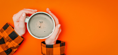 Female's hands holding warm cup of coffee on yellow background. Above viewの写真素材