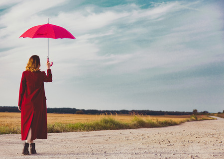 Woman in red coat with umbrella at countryside fieldの写真素材