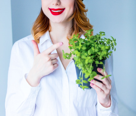 Young redhead woman in hat holding herbs of oregano on grey backgroundの写真素材