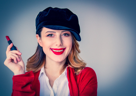 Portrait of young redhead woman in red cardigan and hat with lipstick on grey background. Image made with native lightsの写真素材