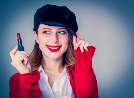 Portrait of young redhead woman in red cardigan and hat with lipstick on grey background. Image made with native lightsの写真素材
