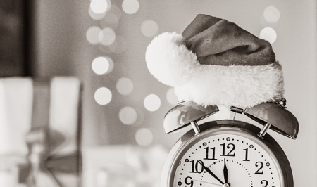 Vintage Alarm clock in Santa Claus hat with Christmas gift and Ligths on background