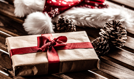 Christmas gift box with Santa Claus hat and pine cones on wooden tableの写真素材