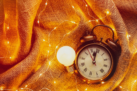 Vintage alarm clock with bulb and Fairy Lights around on jute background. Above point of viewの写真素材