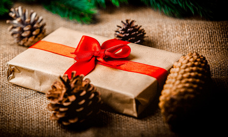 Christmas gift and pine cones on jute background