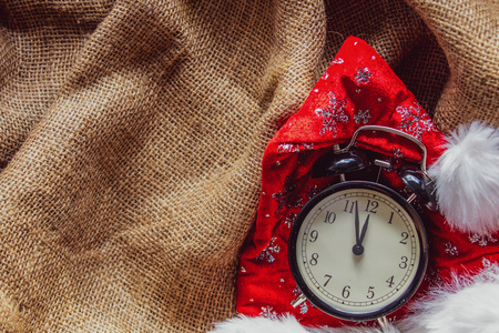 Christmas Santa Claus hat and vintage alarm clock on jute backgroundの写真素材