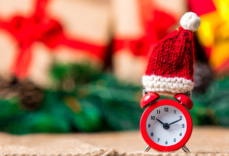 Alarm clock with Santa Claus hat on jute and Christmas gifts on backgroundの写真素材
