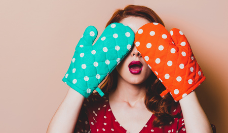 Young redhead housewife with gloves on yellow backgroundの写真素材