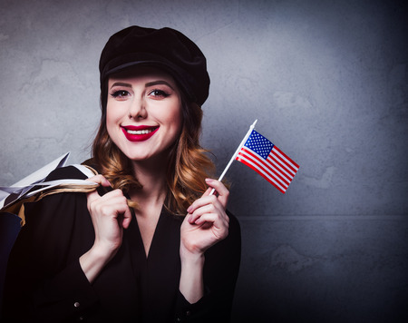 Style redhead girl in hat with shopping bags and flag of the United States of America on grey...
