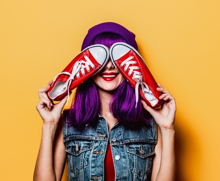 Portrait of young style hipster girl with purple hair and red gumshoes on yellow backgroundの写真素材