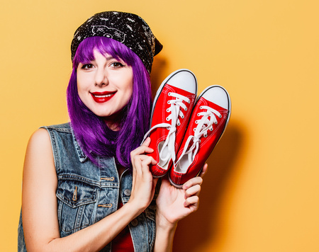 Portrait of young style hipster girl with purple hair and red gumshoes on yellow backgroundの写真素材