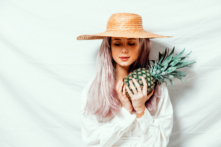 Beautiful caucasian vegan woman in hat with pineapple on white background. Spring time concept and healthy mealの写真素材