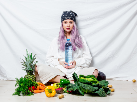 Beautiful caucasian vegan woman with vegetables sitting on a flooor. Spring time concept and healthy mealの写真素材