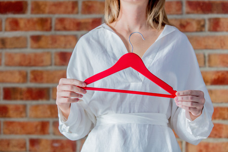 Fashion designer in white shirt holding red hanger on brick wall background. Side view. No faceの写真素材