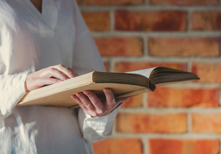 Woman in white shirt holding old book on brick wall backgroundの写真素材
