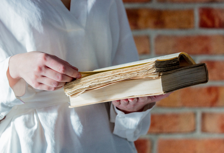 Woman in white shirt holding old book on brick wall backgroundの写真素材