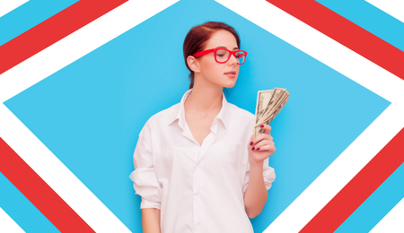 Portrait of redhead woman in red glasses with money on blue backgroundの写真素材