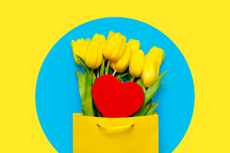 bunch of beautiful yellow tulips in cool shopping bag and heart shaped toy on the wonderful blue backgroundの写真素材
