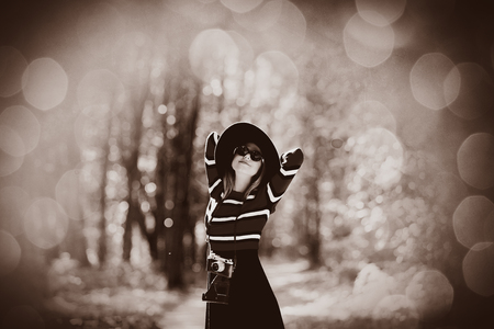 Young girl in a striped sweater with camera and hat in autumn season park . Image in sepia color styleの写真素材