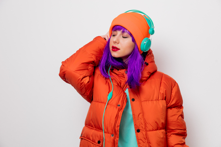 Portrait of a beautiful girl with purple hair in orange hat and jacket and with headphones on white background. Trendy styleの写真素材