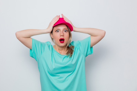 Beautiful young girl in pink cap and blue t-shirt on white background.