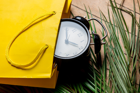 Vintage alarm clock in yellow bag and palm leaves on wooden table. Above viewの写真素材