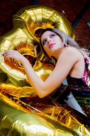 Young woman with golden balloons on her thirty years birthday. Indoor location. Person is in vintage 80th dress and hairstyle. At homeの写真素材