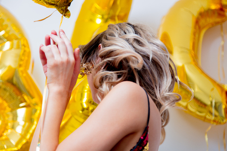 Young woman with golden balloons on her thirty years birthday. Indoor location. Person is in vintage 80th dress and hairstyle. On white backgroundの写真素材