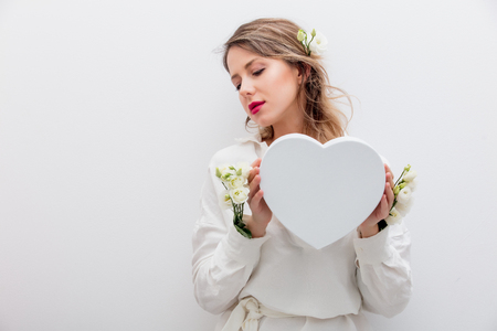Beautiful woman with white roses dressing in a white shirt holding a heart shape gift box. Springtime concept or Valentines Day holidayの写真素材