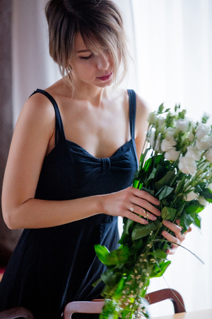 A girl dressed in a black dress is holding white roses in a bouquet before putting them in a vase. Sprint time conceptの写真素材