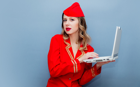 Portrait of charming vintage stewardess wearing in red uniform with laptop computer. Isolated on gray background.の写真素材