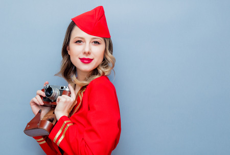 Portrait of charming vintage stewardess wearing in red uniform with vintage camera. Isolated on gray...