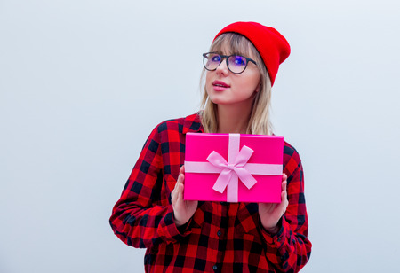 Young woman in red shirt and hat holding holiday gift box on white background. Isolated