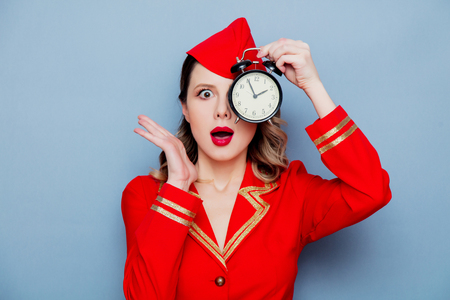 Portrait of charming vintage stewardess wearing in red uniform with alarm clock. Isolated on gray...
