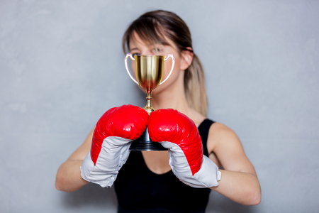 Young woman in boxing gloves with golden cup on gray background. 90s flashlight styleの写真素材