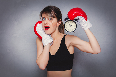 Young woman in boxing gloves with alarm clock on gray background. 90s flashlight styleの写真素材