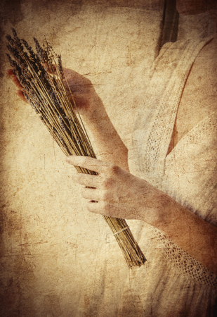 Woman in white dress holding lavender in hands and stay near window. Image in high key styleの写真素材