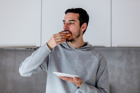 Man eating donut on breakfast at kitchen at home.の写真素材