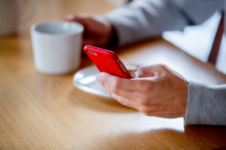 Young handsome man sitting at table with cup of coffee or tea and mobile phone. Kitchen location in morningの写真素材