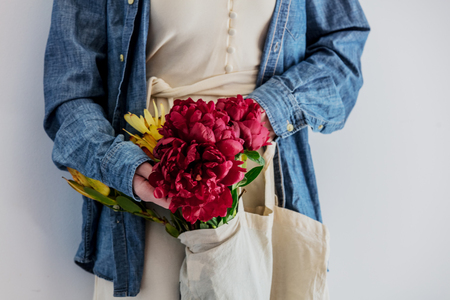 Female hands holding bouquet of peonies and  Leucadendron in a tote bag on white background. wearing a denim shirtの写真素材