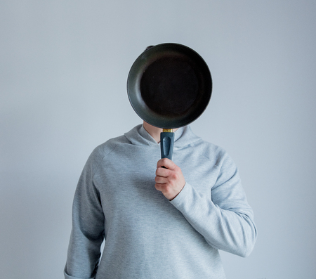 Man in gray hoody holdng pan at face level on white backgroundの写真素材