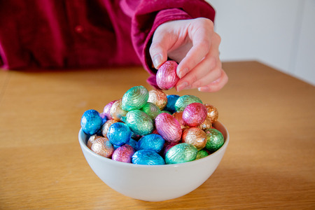 female hands try to take Easter eggs in plate on a wooden table at kitchen in home