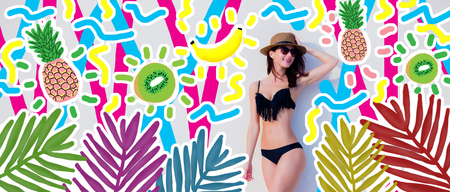 Beautiful girl in sunglasses, hat, black bikini on background with kiwi, bananas and pineapples.