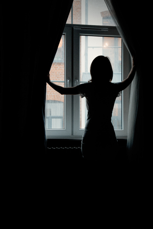a young girl looks behind the curtains in the window in the morningの写真素材