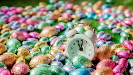 color Chocolate Easter eggs and alarm clock on green spring grass